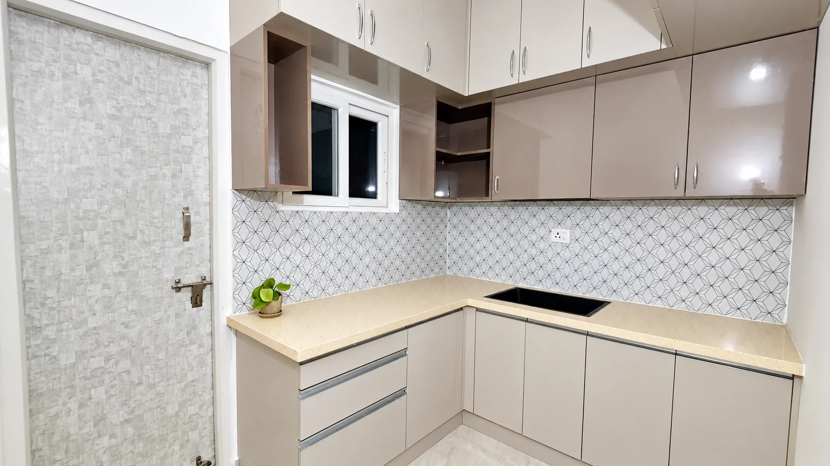 Swarna Griha – 3 Serene Highlands modular kitchen with beige high-gloss cabinets, a geometric tile backsplash and cream worktop