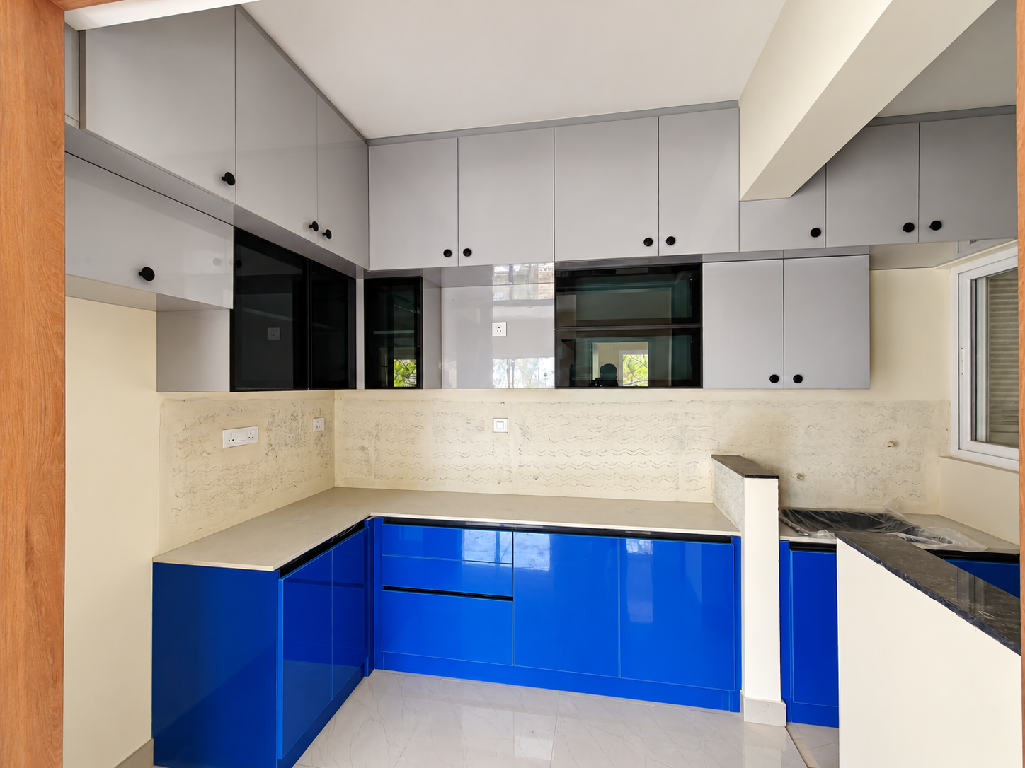 Gokul project modular kitchen with royal blue base units, grey wall cabinets and black glass lofts