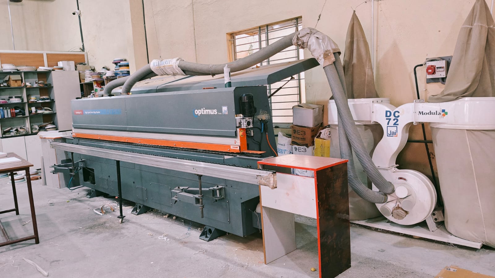 Automatic edge banding machine with edge-band rolls on shelves at the CMS Interiors factory.