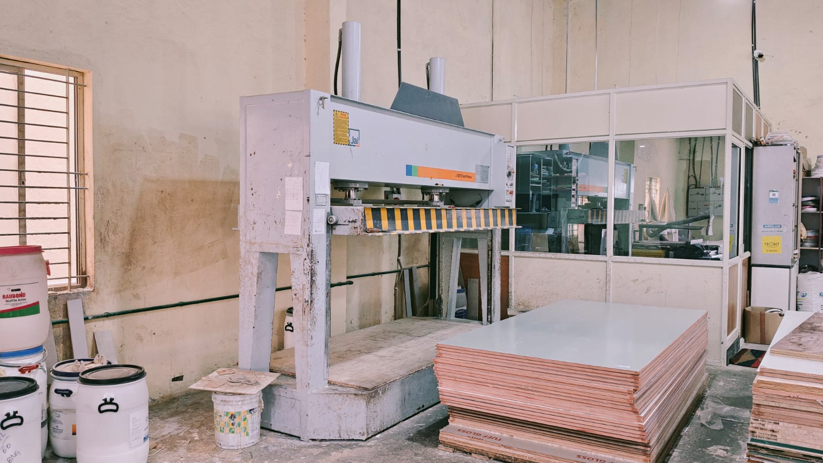 Cold press beside stacked laminated panels at the CMS Interiors factory.